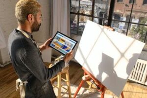 Un homme devant une toile vierge de peinture, a dans les mains une tablette avec des graphiques dessus